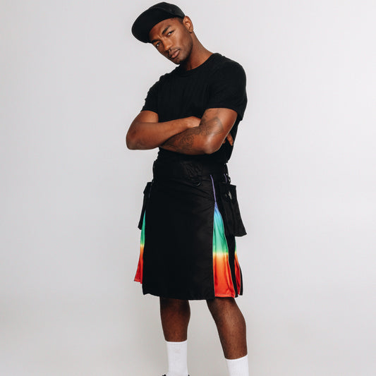 A model wearing a black t-shirt, black kilt with vibrant rainbow-colored side panels, white socks, and black sneakers, posed against a solid light gray background.