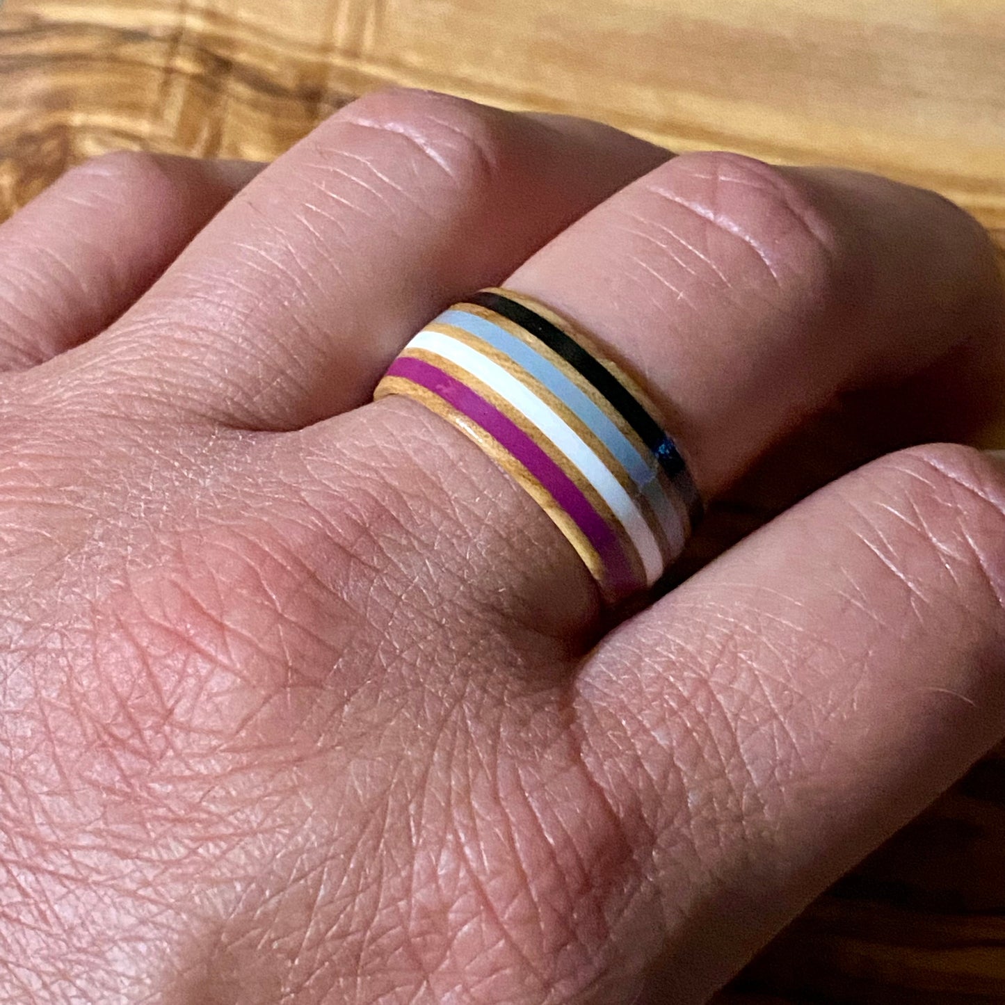 Hand wearing a ring with asexual pride stripes on a wooden surface