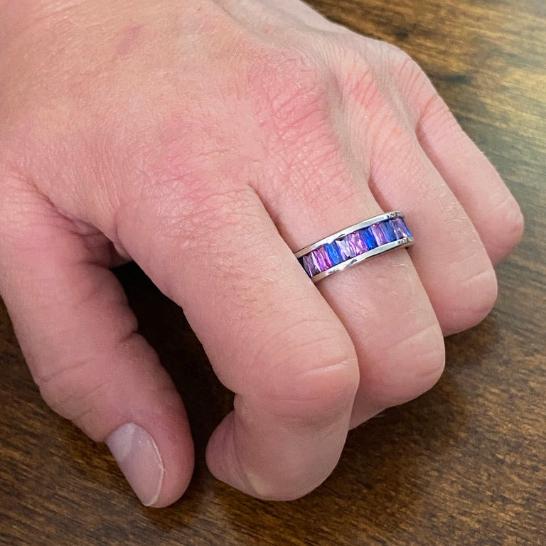 Hand wearing a bisexual pride colored gemstone ring on a wooden surface
