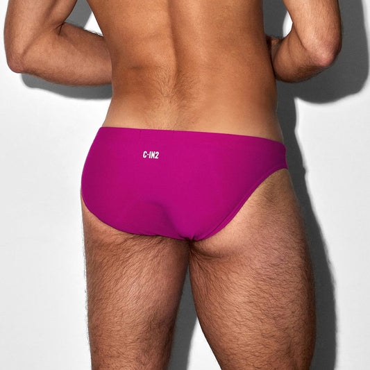 Person wearing bright pink swim briefs with 'C-IN2' branding on a light gray background
