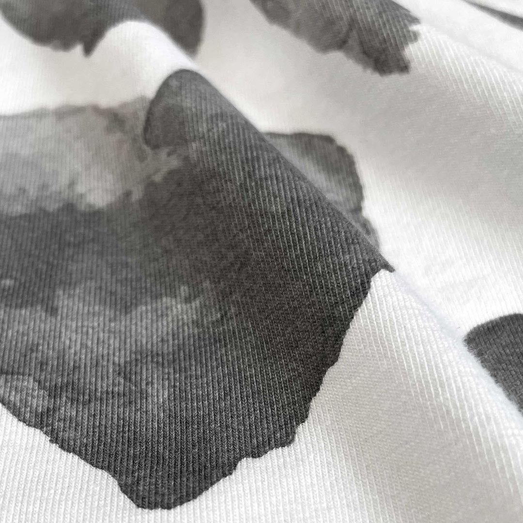 A close-up of a white knit fabric with a large dark gray watercolor-style heart patch on top.