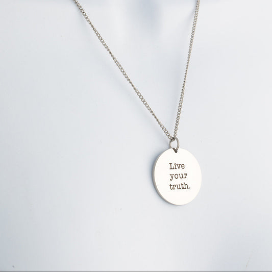 Silver necklace with a pendant that says 'Live your truth' on a light gray background