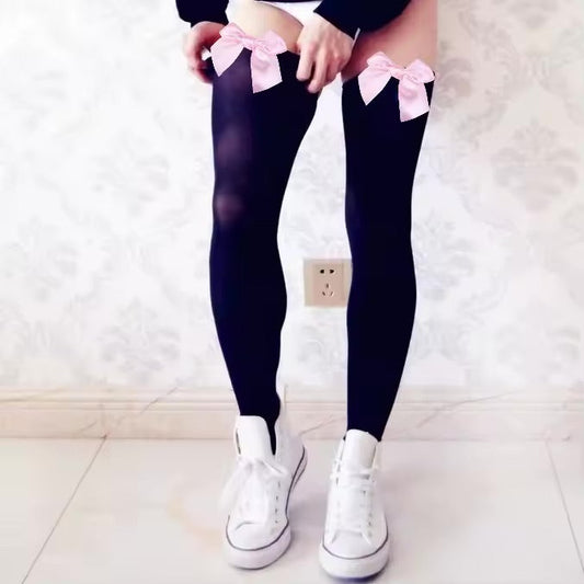 Black stockings with pink bows worn by a man, standing on a light-colored floor.