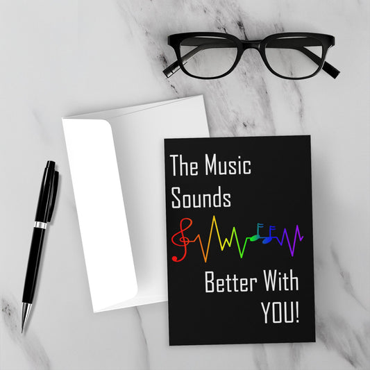 Greeting card with lgbtq rainbow musical notes and text on a marble surface with glasses and pen.