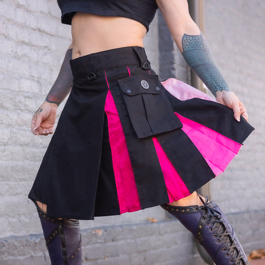 Person wearing a black and pink skirt with tattoos on arms and legs.