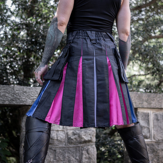 Person wearing a black and trans color striped kilt with tattoos on arms, standing outdoors.