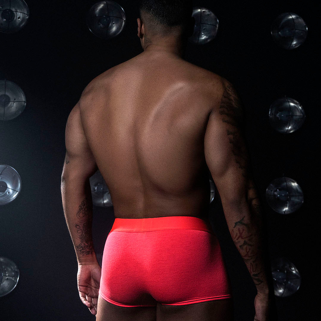 Man wearing red underwear against a dark background with light sources.