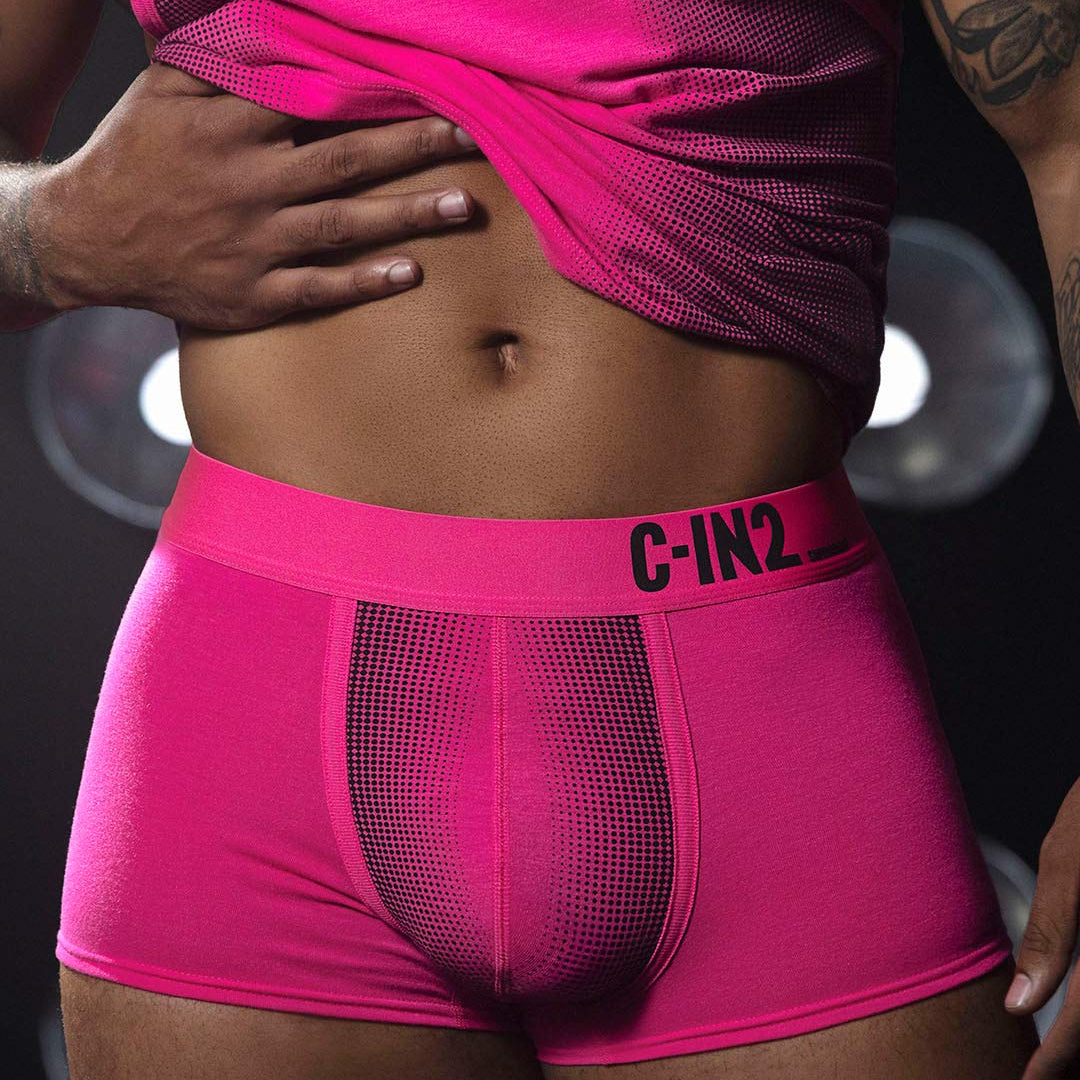 Person wearing bright pink underwear with 'C-IN2' brand logo, against a dark background.