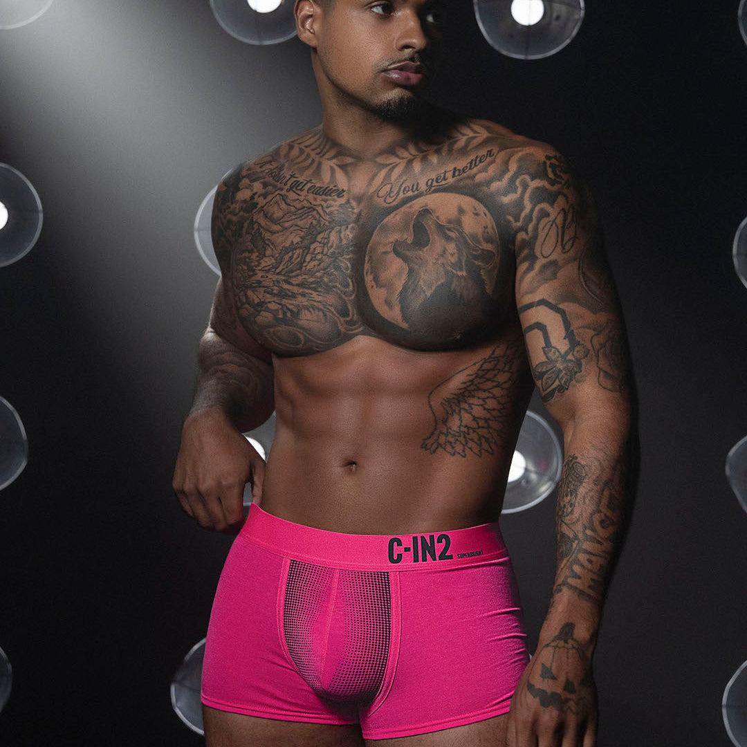 Man wearing pink underwear with visible tattoos against a dark background