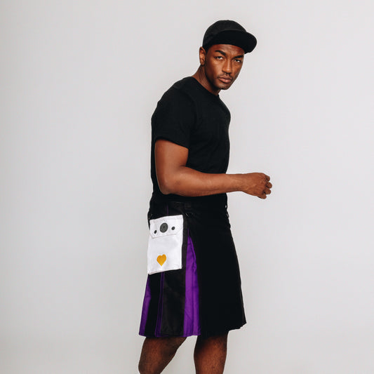 Person wearing a black t-shirt, black kilt with a purple accent, and a cap on a white background