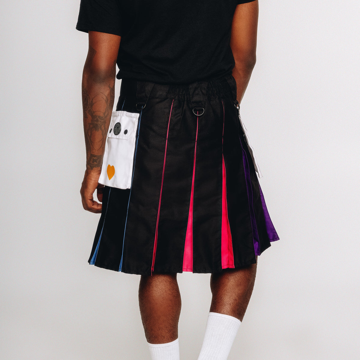 Person wearing a black kilt with polyamory colored accents on a white background