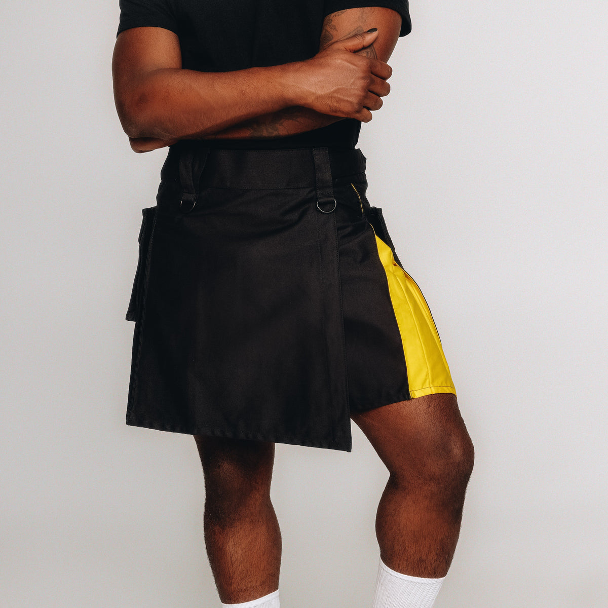 Person wearing a black and yellow kilt with white socks and black shoes on a plain background