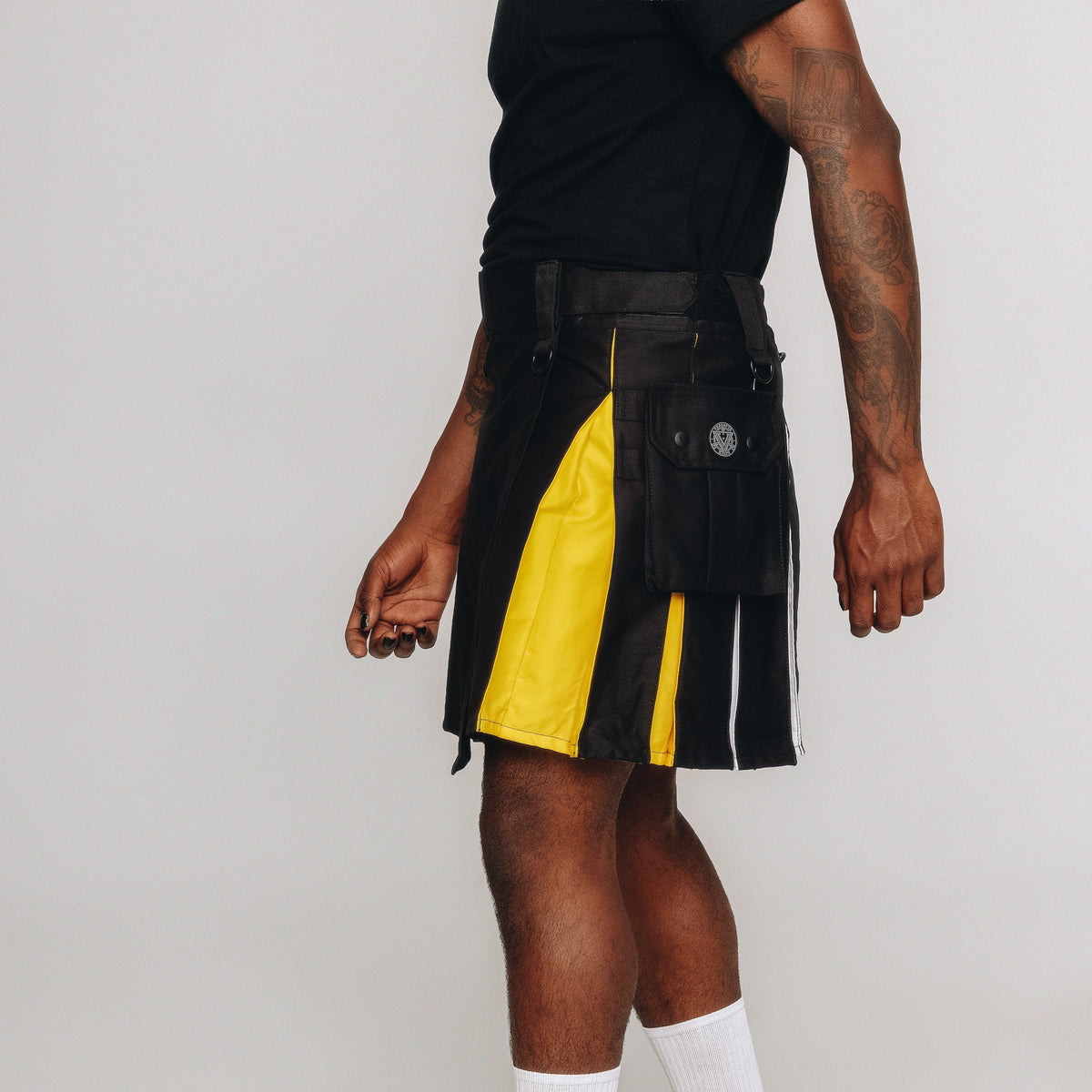 Person wearing a black and yellow kilt with white socks and black shoes on a plain background