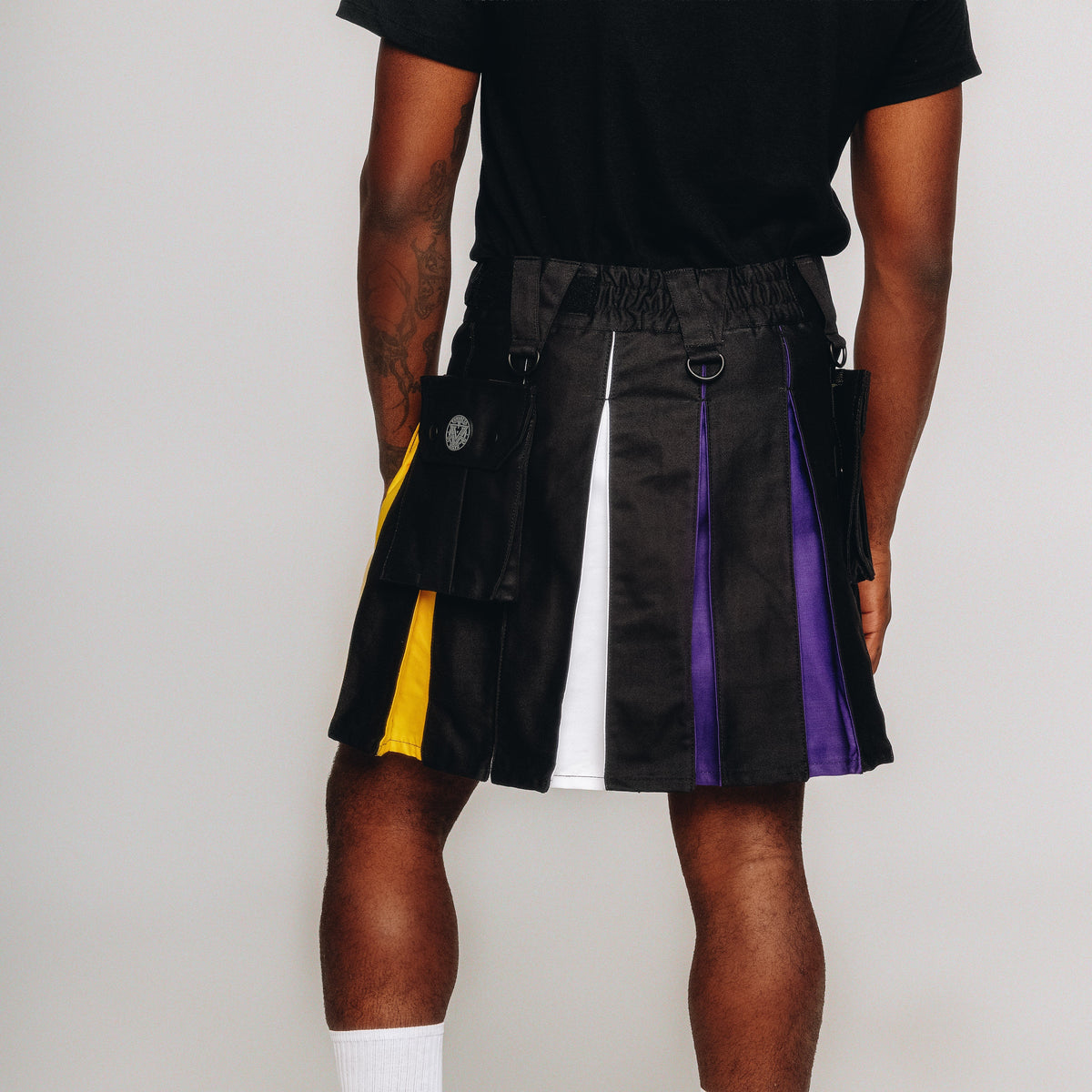 Person wearing a black kilt with non-binary pride inspired accents on a white background