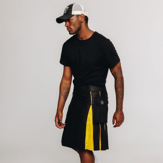 Person wearing a black kilt with nonbinary pride colored pleats and black cap on a white background