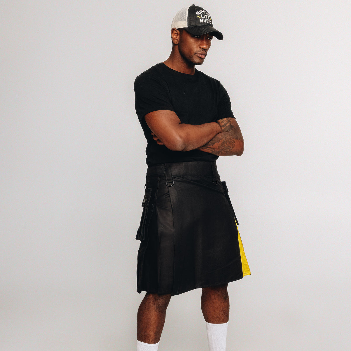 Person wearing a black kilt with nonbinary pride colored pleats with a white background