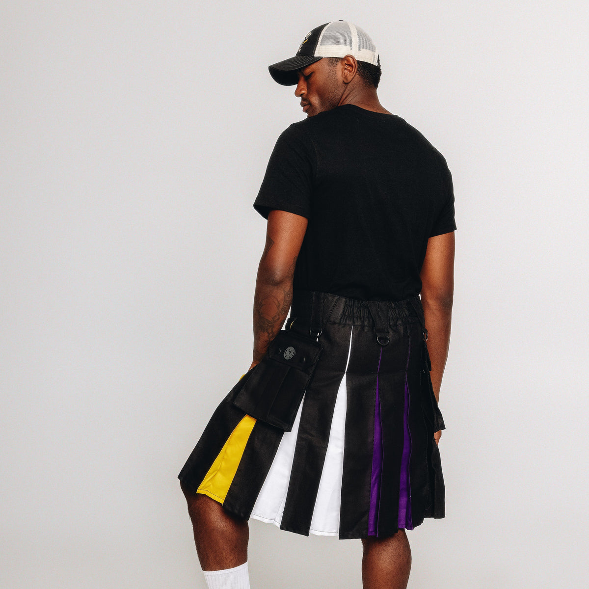 Person wearing a black kilt with nonbinary pride colored pleats on a white background