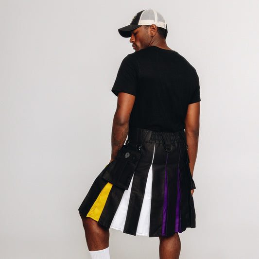 Person wearing a black kilt with nonbinary pride colored pleats on a white background
