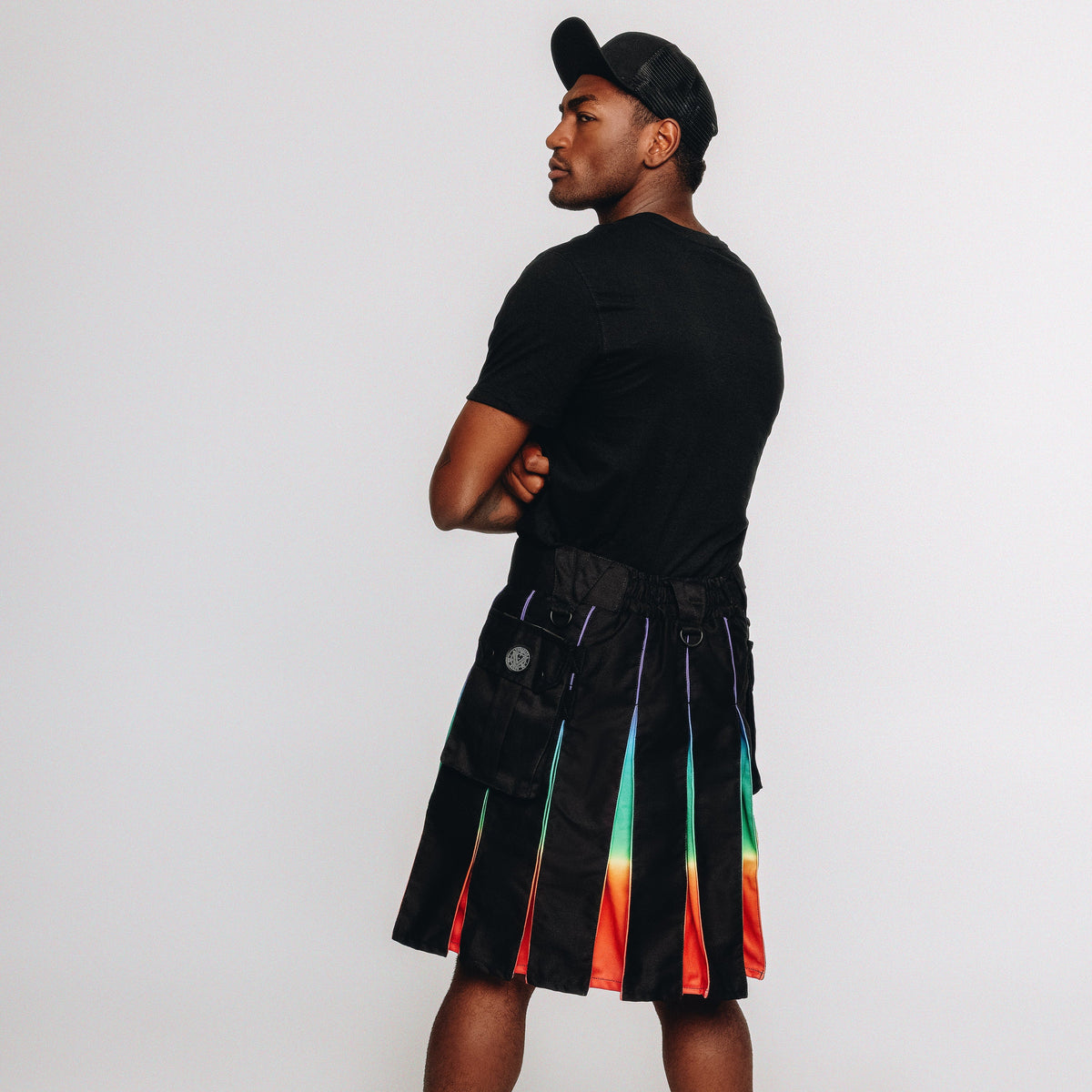 Person wearing a black t-shirt and black kilt with rainbow pleats on a white background