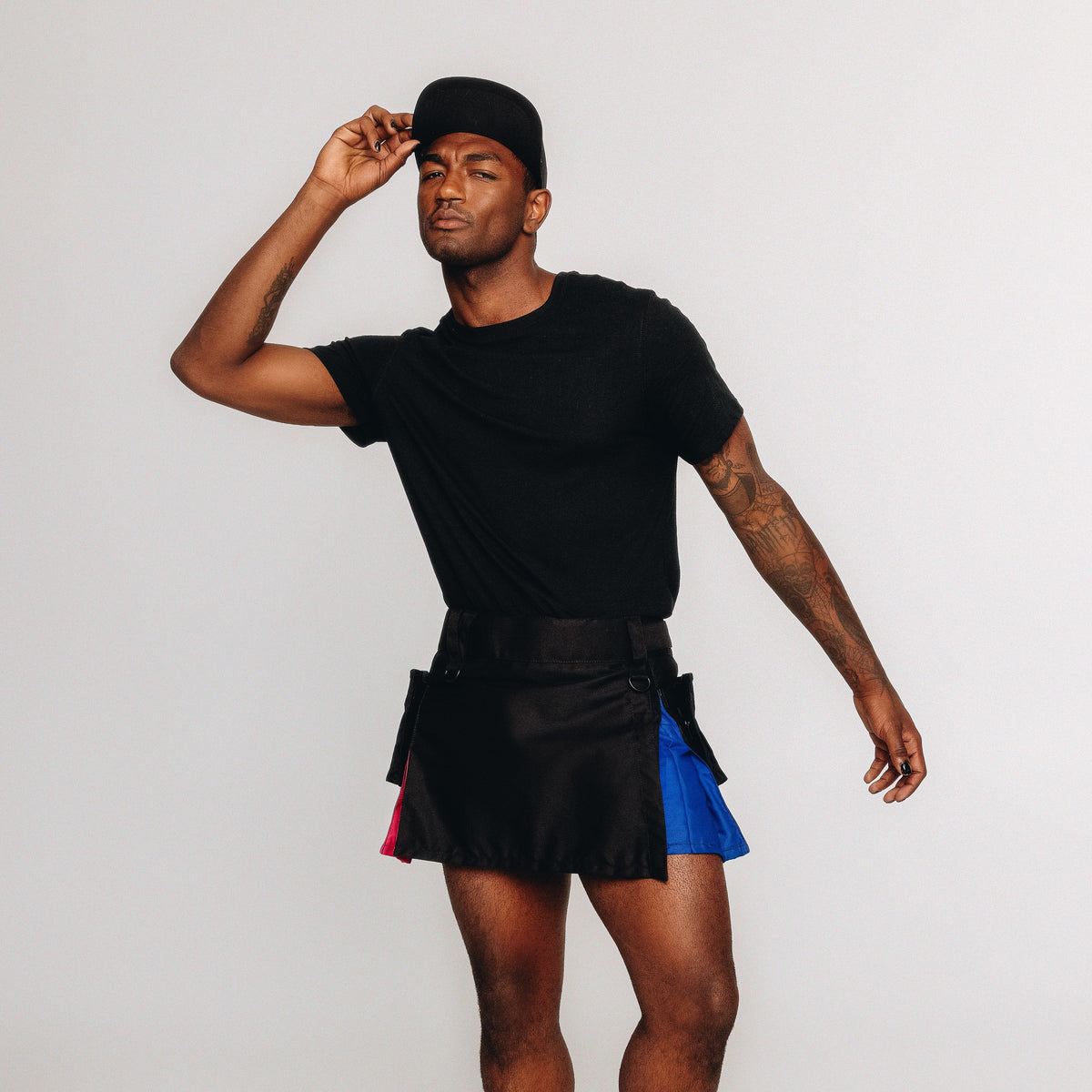Person wearing a black kilt with bi pride colored accents on a white background