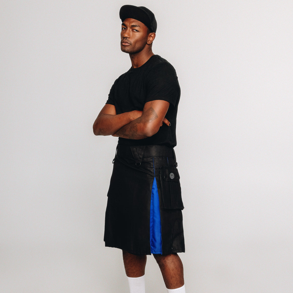 Person wearing a black t-shirt, black and rainbow kilt, white socks, and black shoes on a white background