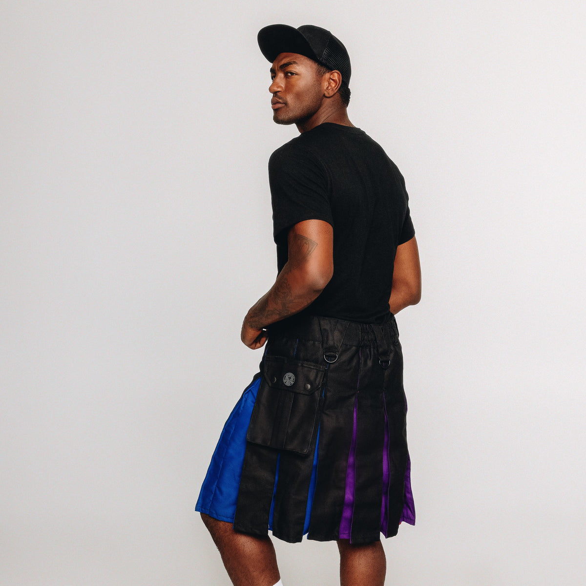 Person wearing a black t-shirt, black kilt with rainbow accents, white socks, and black shoes on a white background.