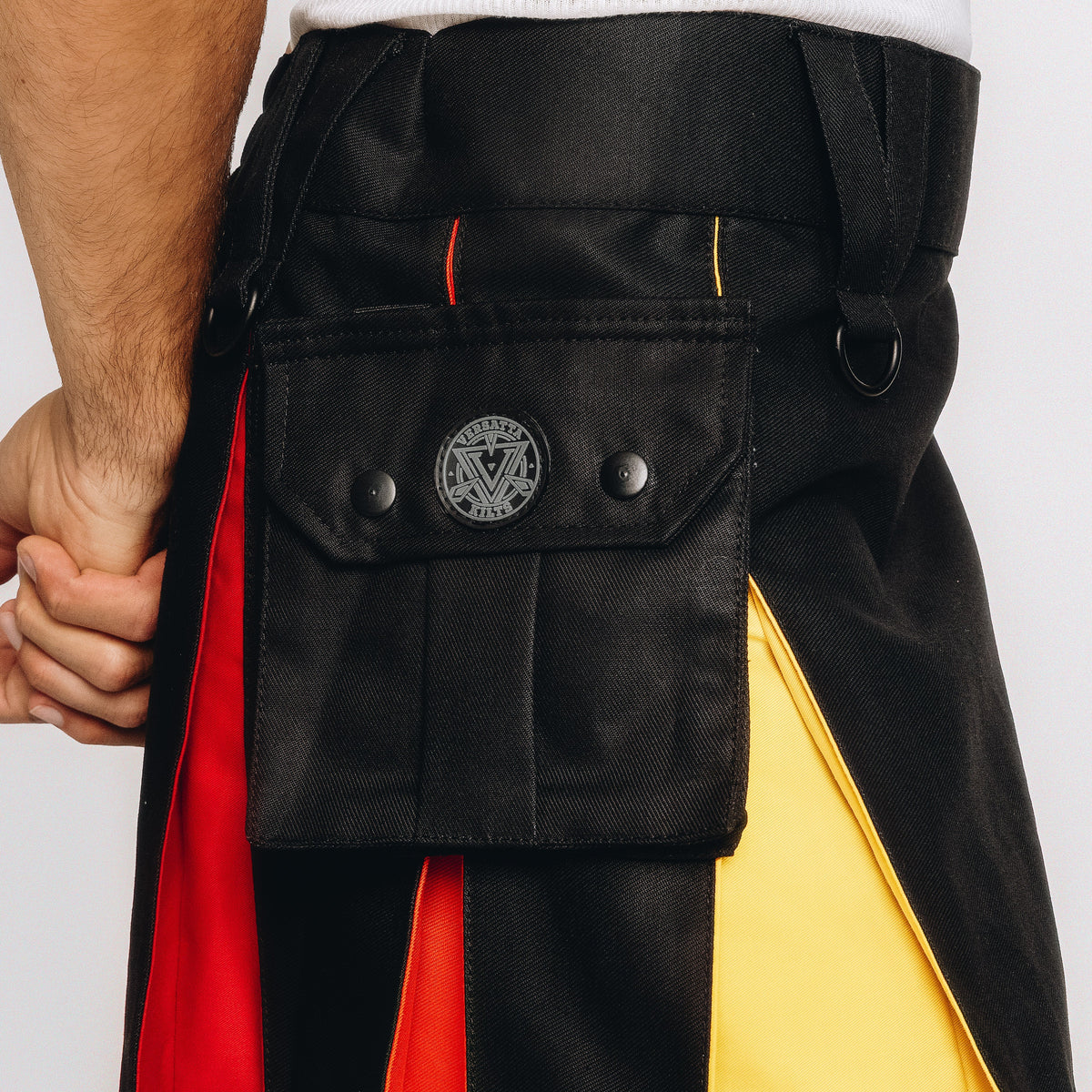Close-up of a person wearing a black kilt with bold red, orange, and yellow color-block panels and a front flap pocket with metal snaps.