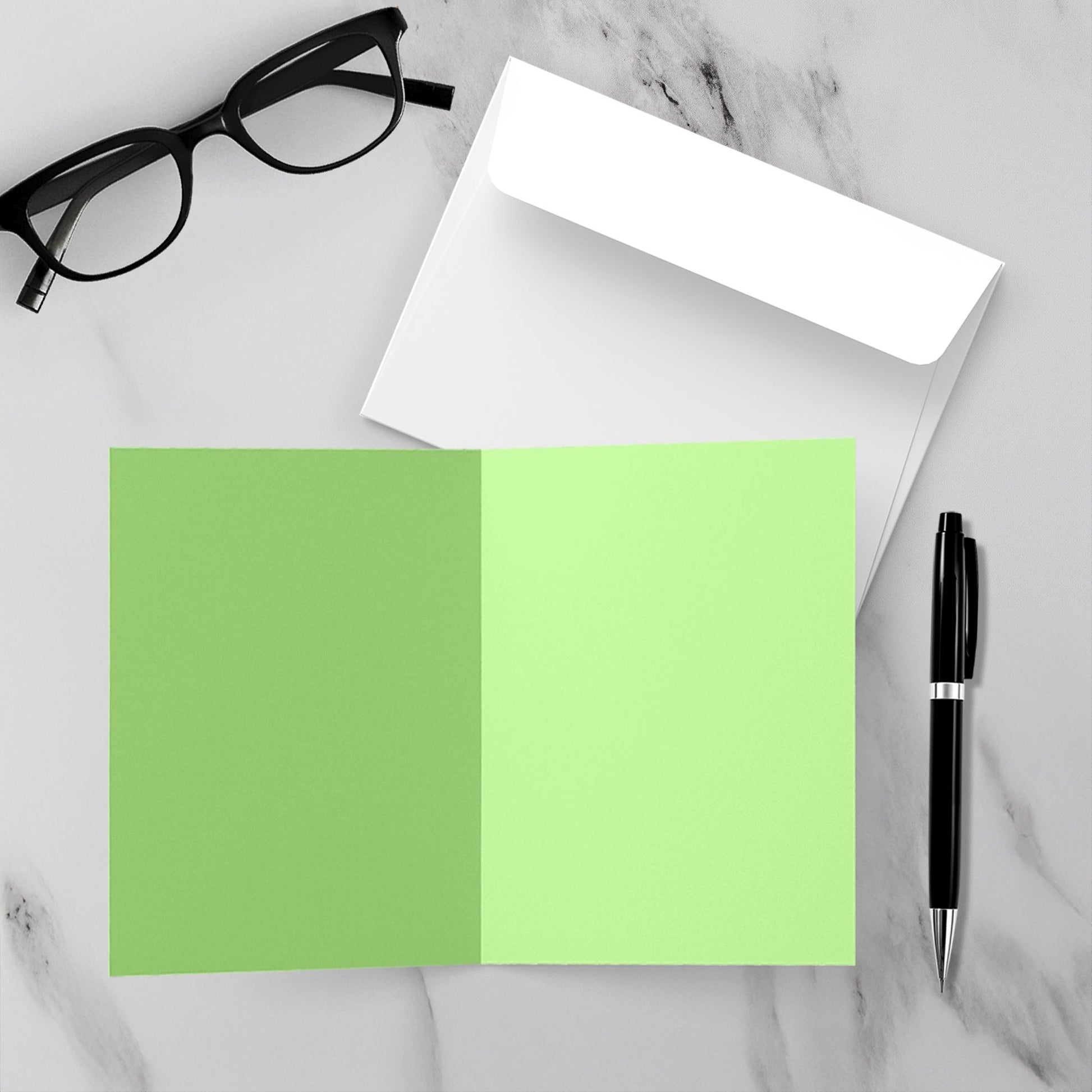 Green inside blank card with a pen and glasses on a marble surface