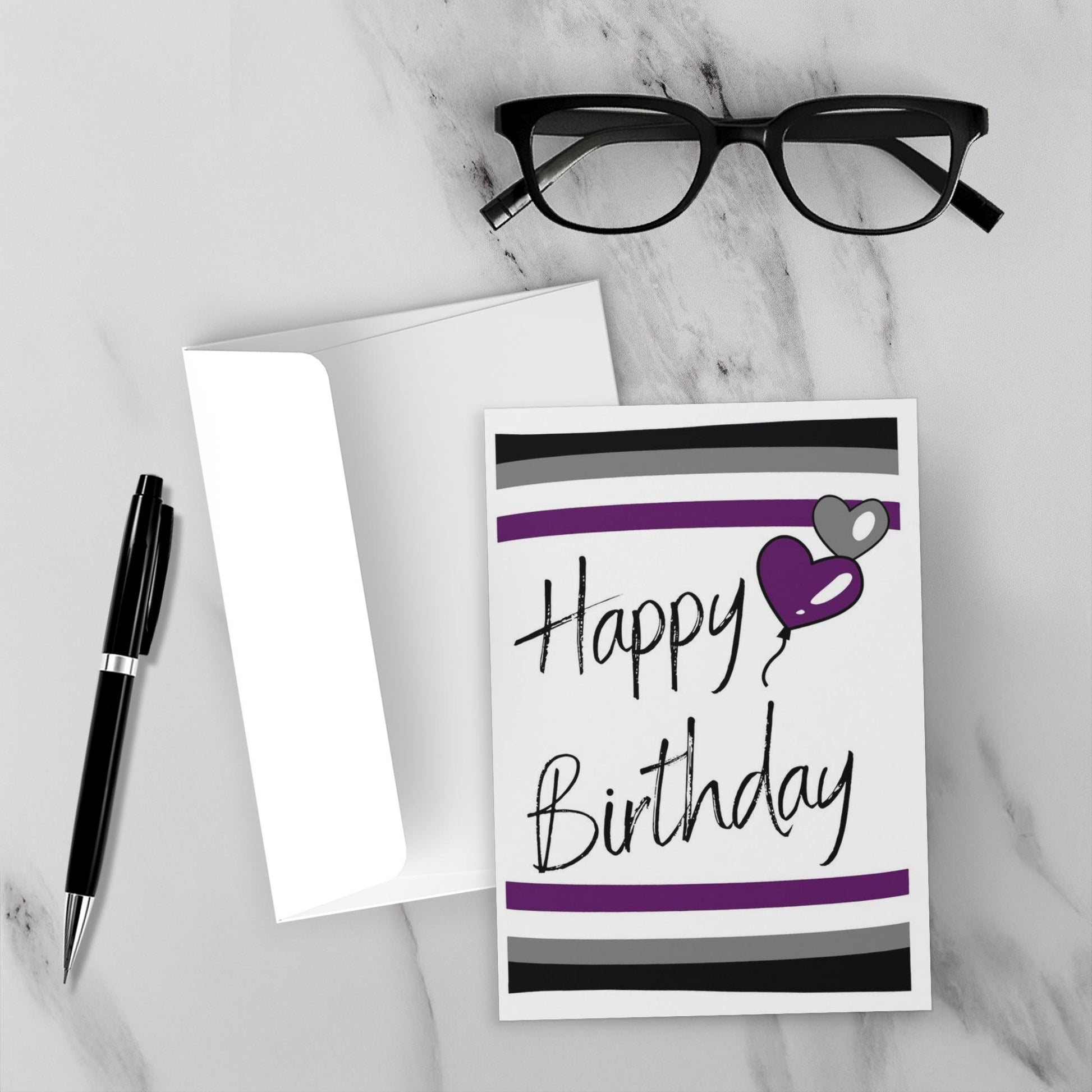 Birthday card with purple heart and 'Happy Birthday' text on a marble surface with glasses and pen.