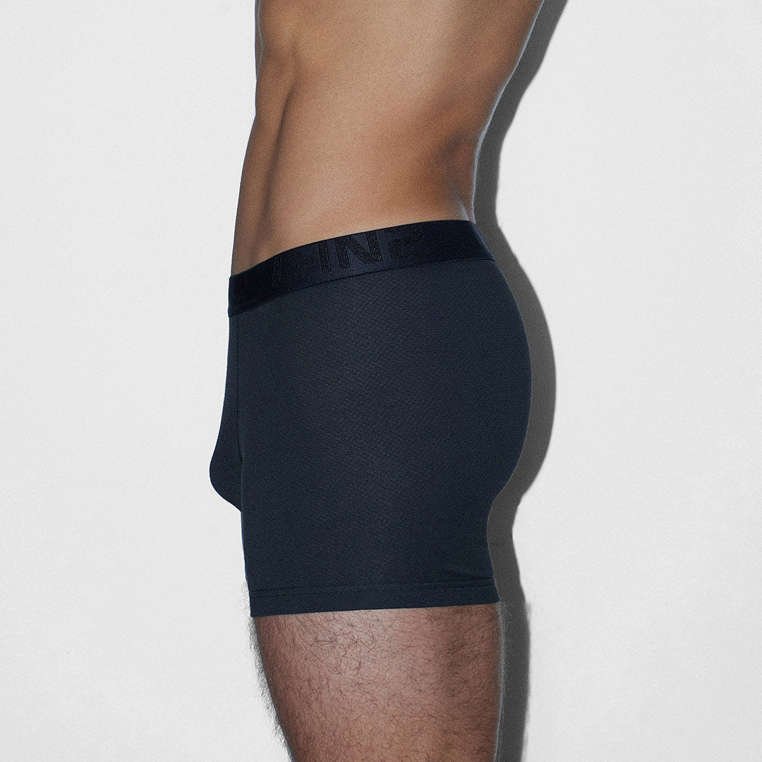 A side profile view of a man wearing dark navy blue boxer briefs against a light gray background.