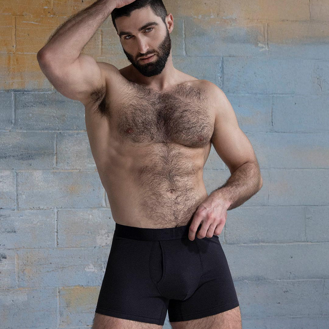 Man wearing black underwear against a textured wall.