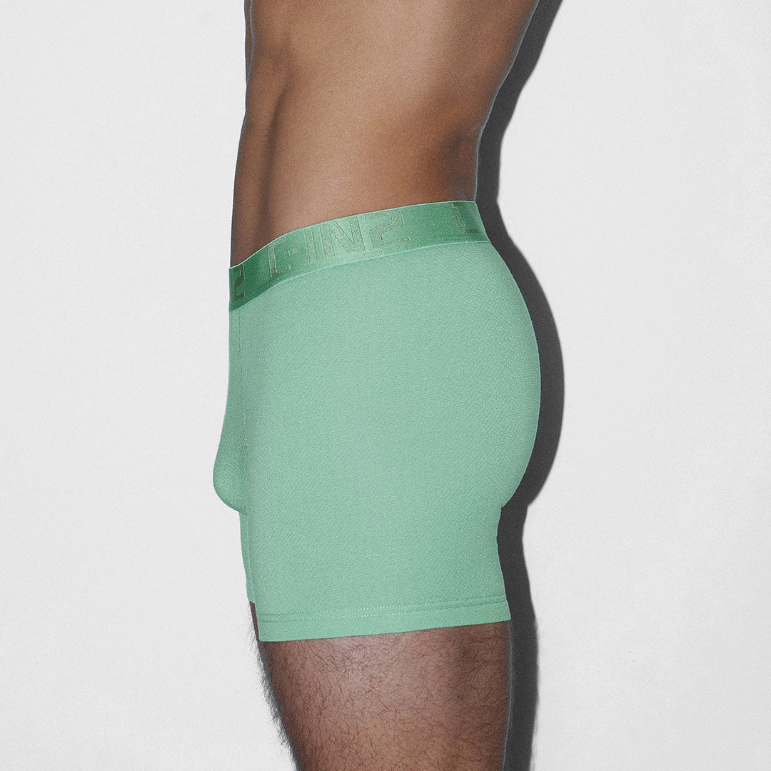 A side profile view of a model wearing sage green boxer briefs against a plain light gray background.