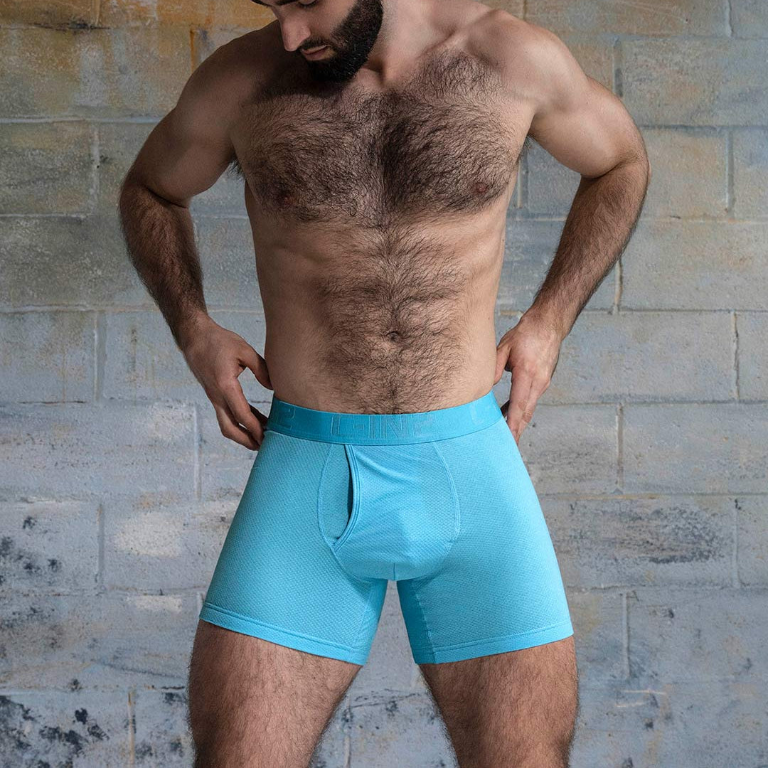 Man wearing turquoise boxer briefs against a stone wall background