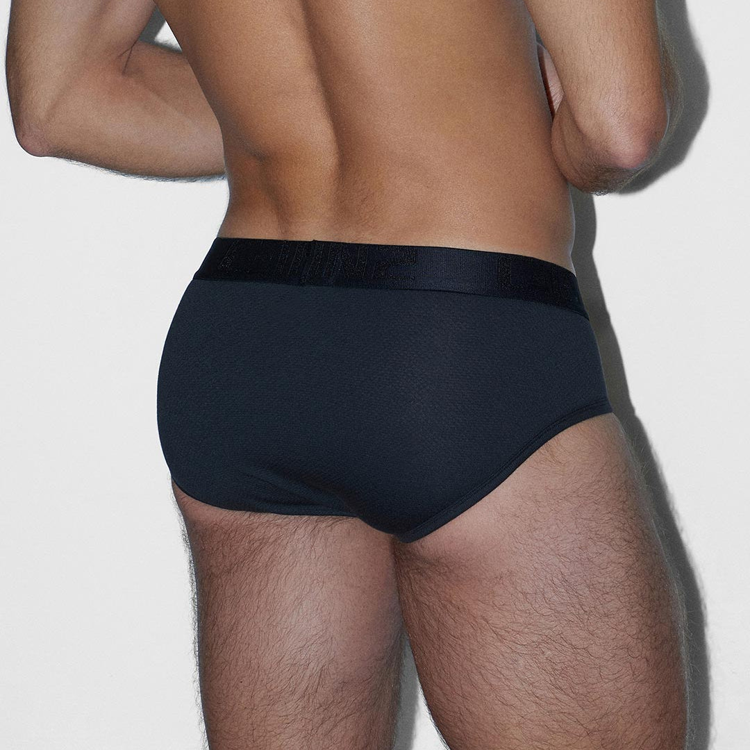 Rear view of a man wearing black briefs against a plain light gray background.