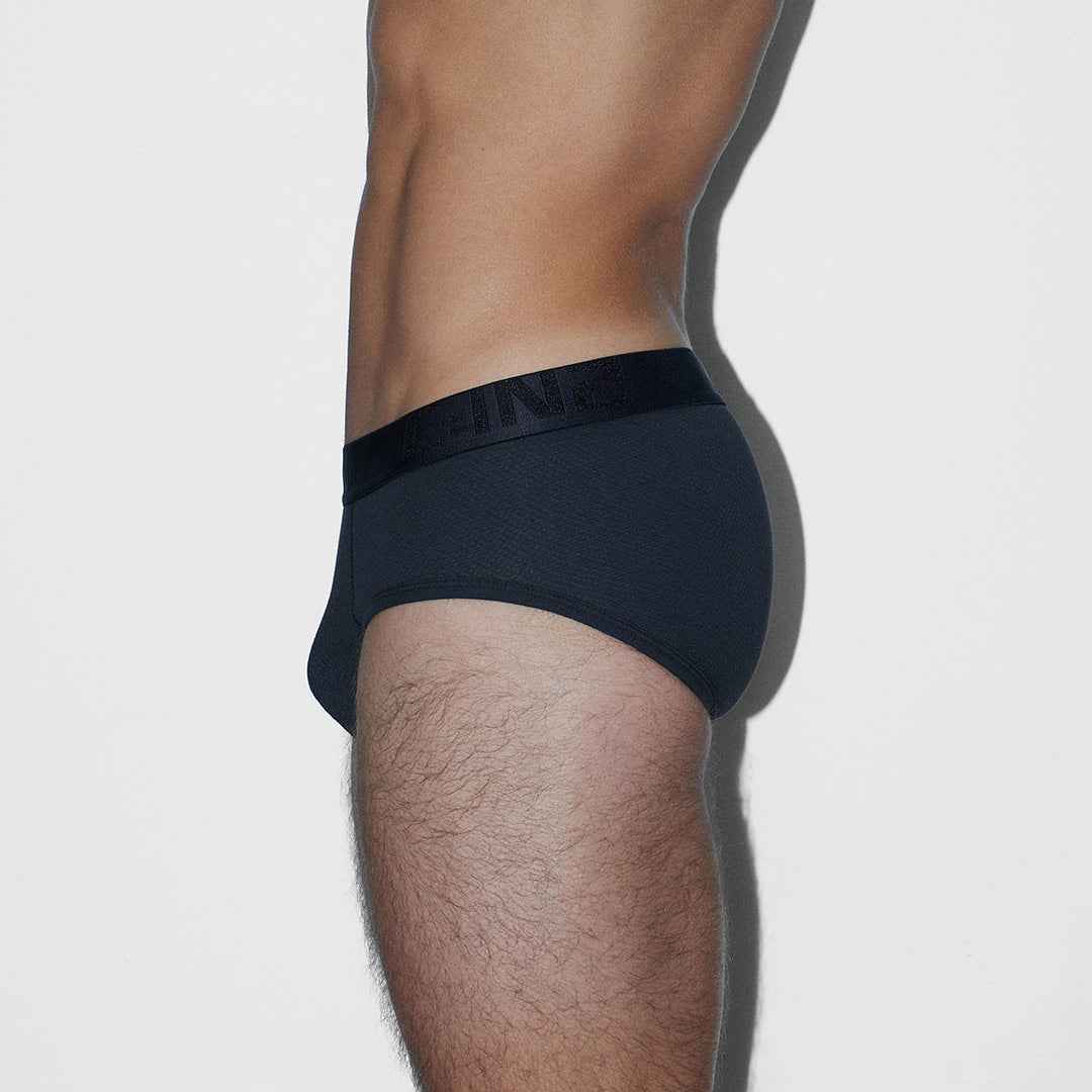 A side profile view of a man wearing black briefs with a wide black waistband featuring the embossed brand name 'C-IN2'.