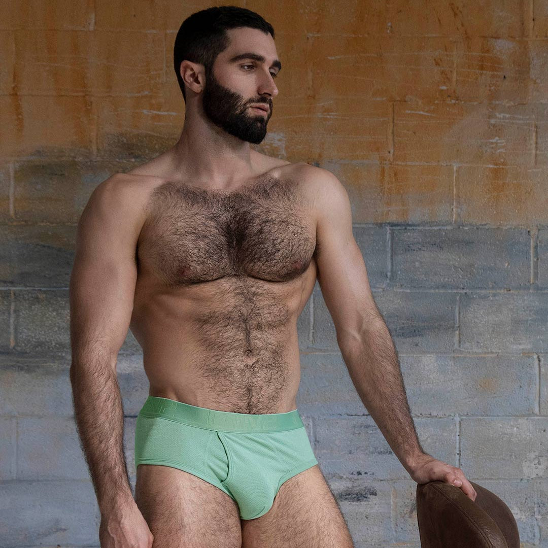Man wearing green underwear standing against a stone wall.