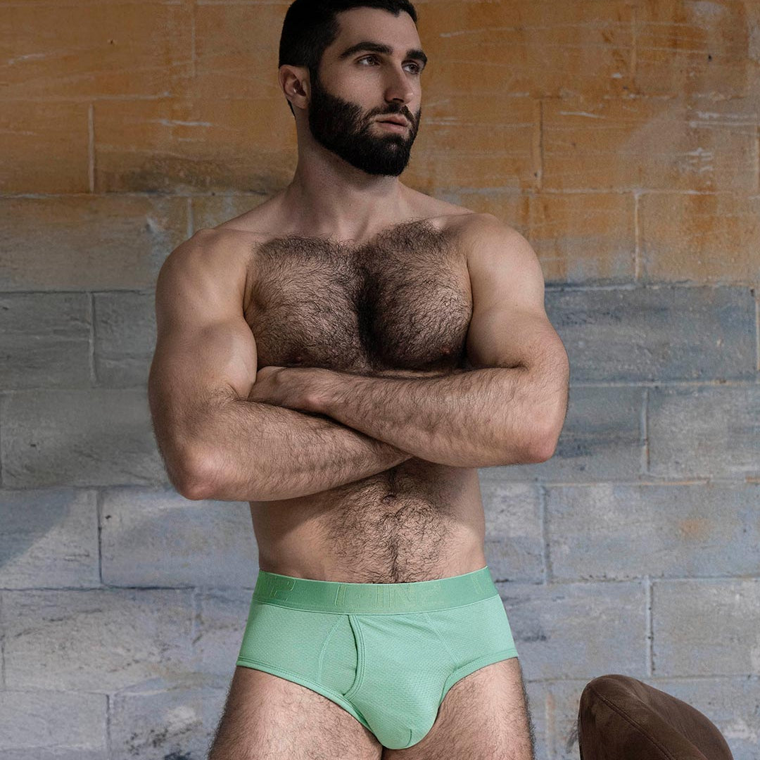Man wearing a green underwear set against a textured wall.