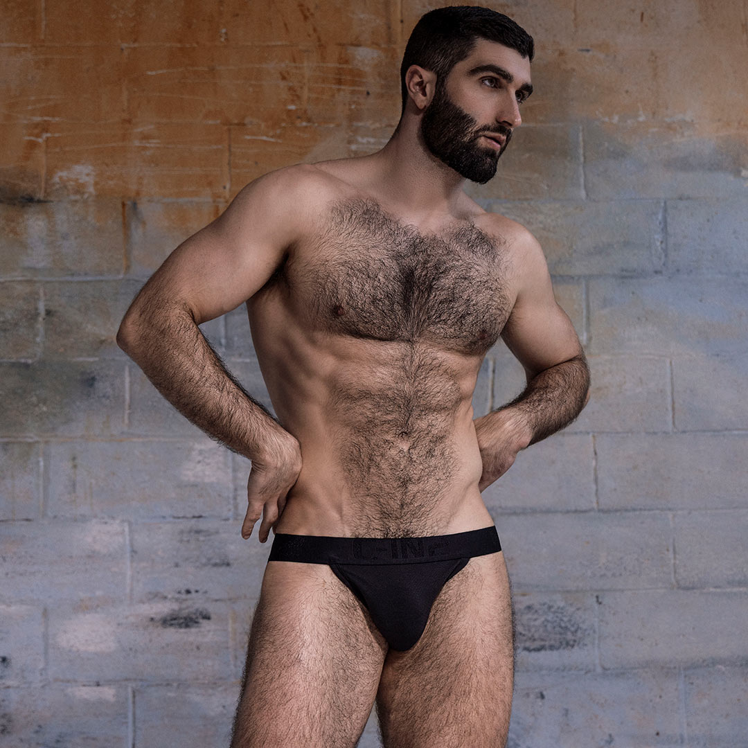 Man wearing black underwear with C-IN2 branding against a textured wall.