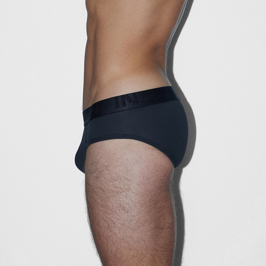 A side profile view of a man wearing black briefs, showing the side waistband with tonal 'C-IN2' branding.