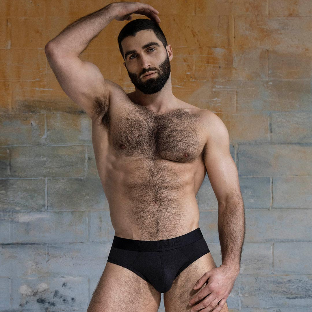 Man wearing a black underwear against a textured wall.