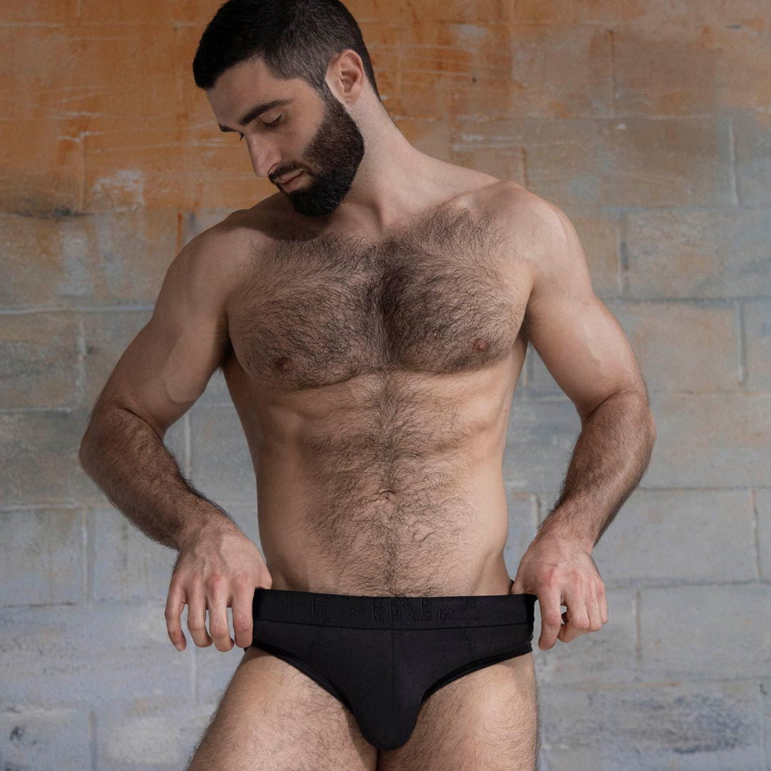 Man wearing a black underwear against a textured wall.