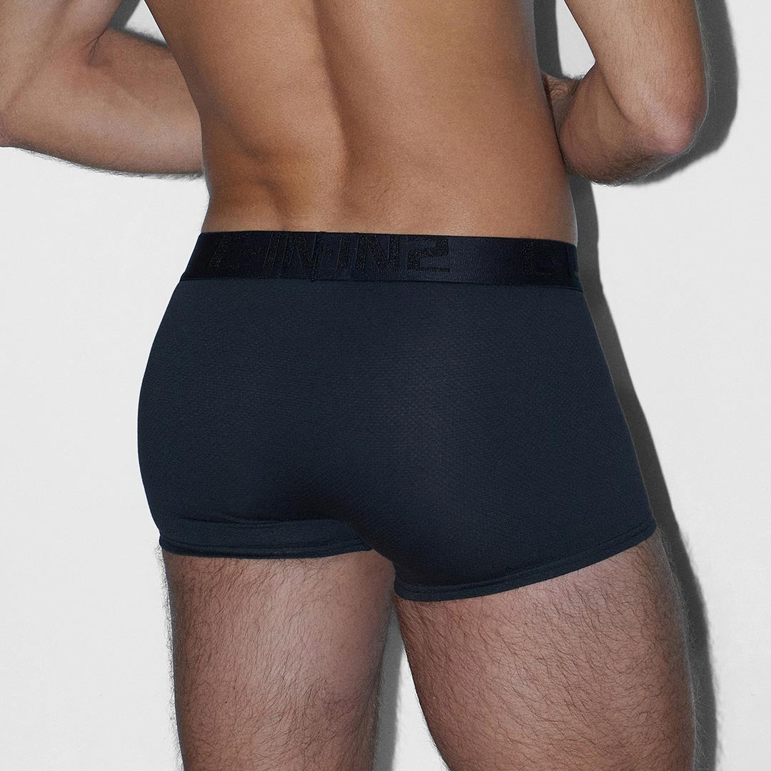 Rear view of a man wearing black boxer briefs with a black elastic waistband on a light gray background.
