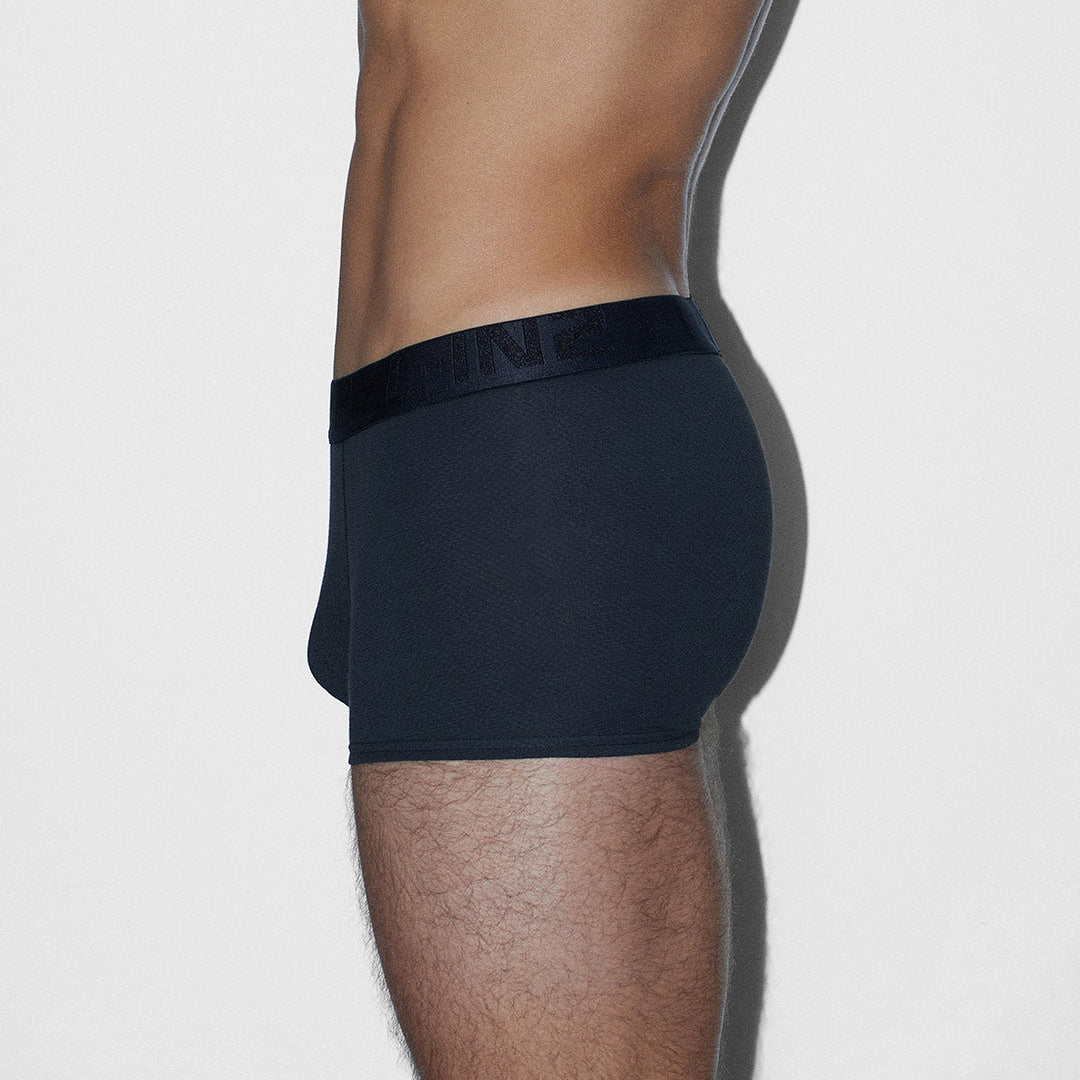 A side profile view of a man wearing black boxer briefs against a light gray background.
