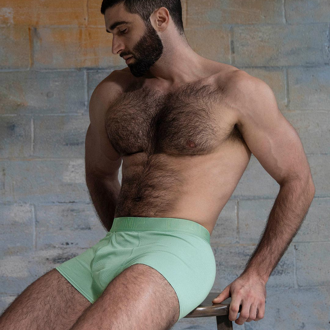 Man wearing light green underwear against a textured wall.