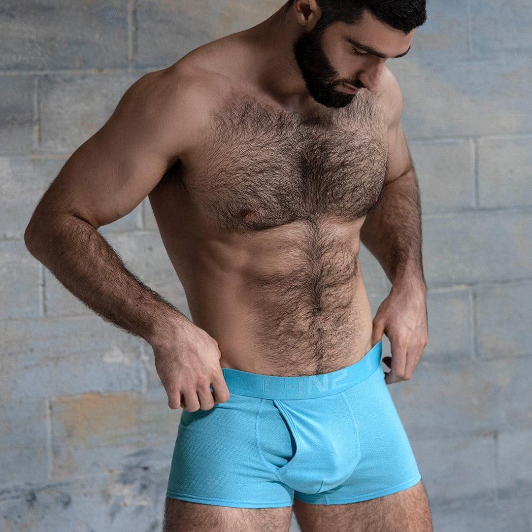 Man wearing light blue boxer briefs against a textured wall background
