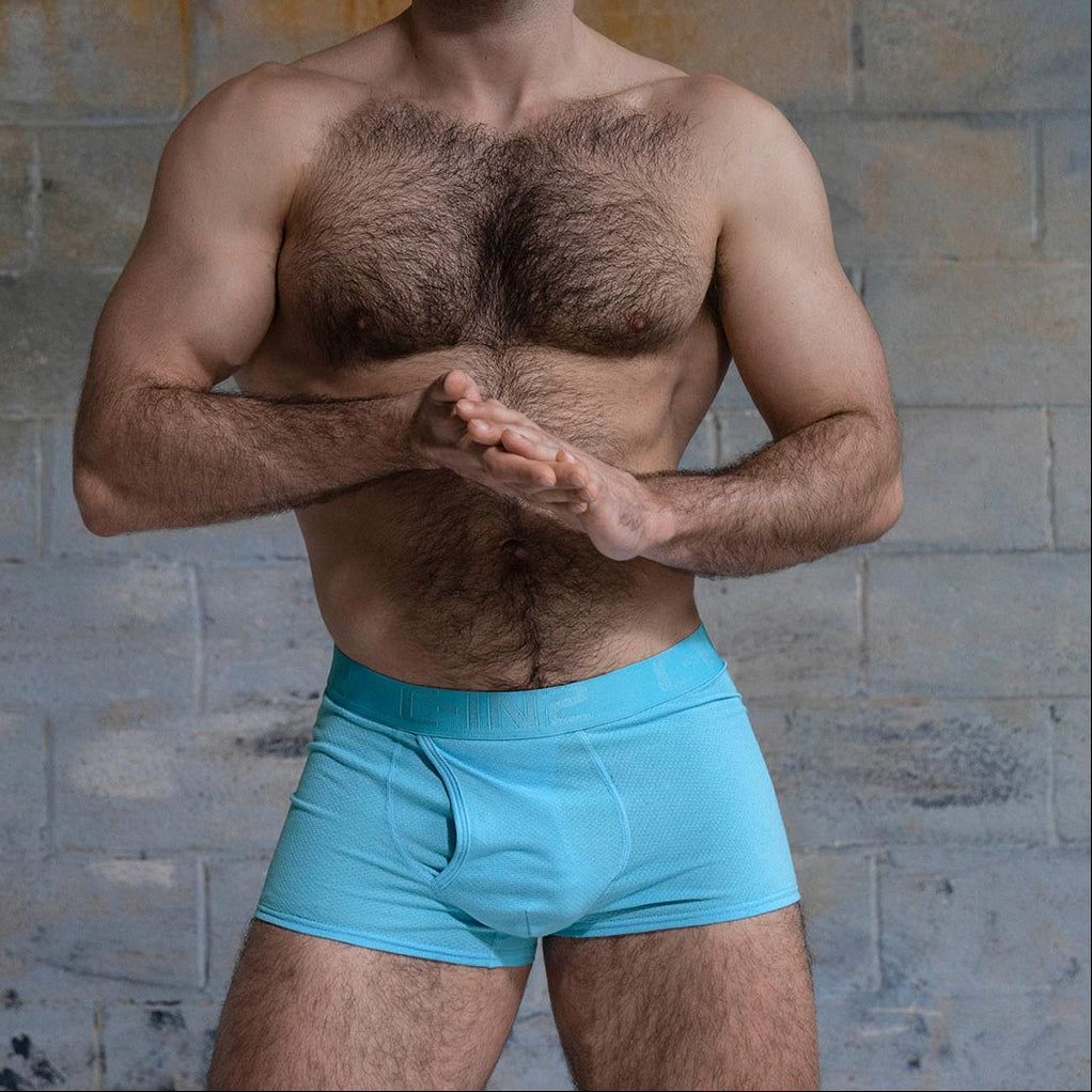 Man wearing light blue boxer briefs against a textured wall background