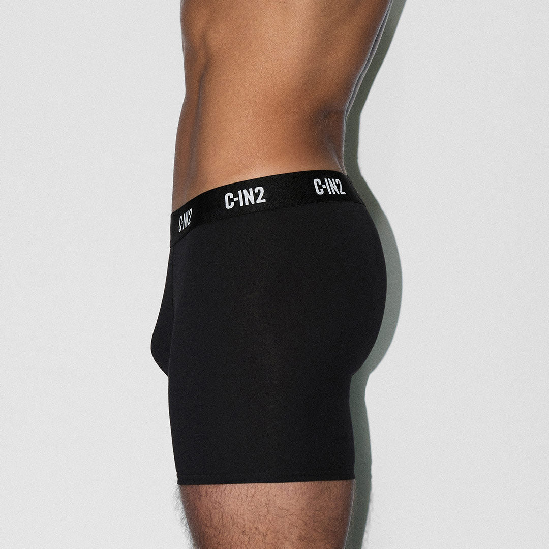 A side profile of a male model wearing black boxer briefs with a black waistband featuring white 'C-IN2' branding, set against a plain light gray background.
