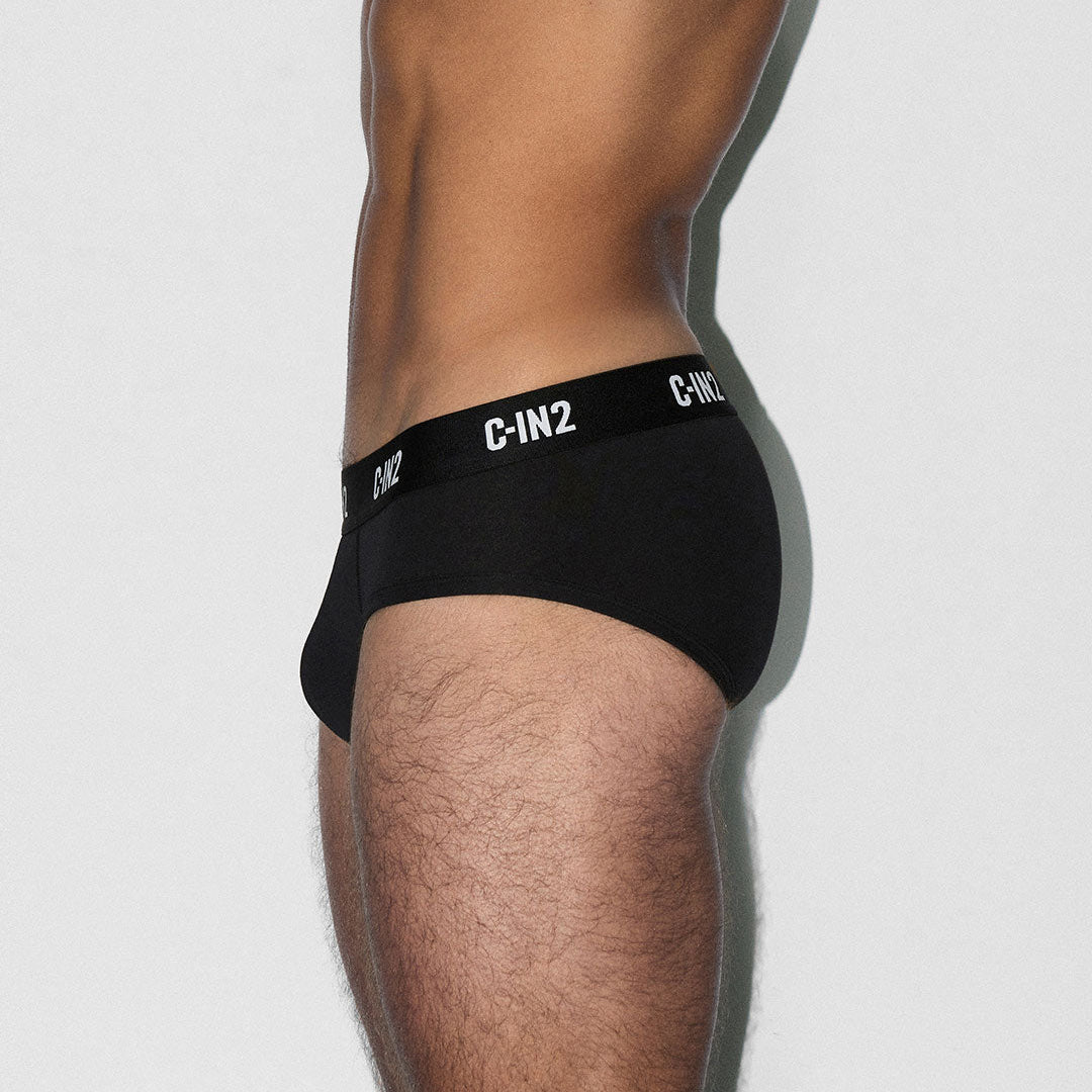 Side view of a man wearing black C-IN2 men's briefs, showing the side profile of the waistband with white branding text.