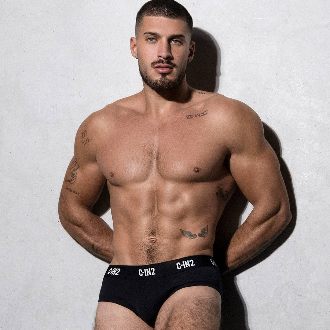 Muscular man wearing black underwear with visible branding against a plain background