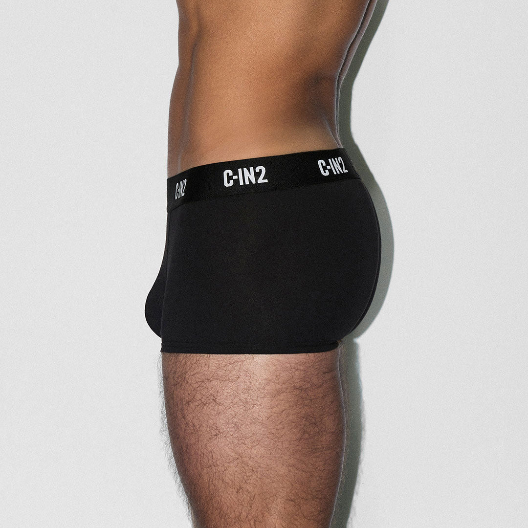 A side profile view of a man wearing black C-IN2 boxer briefs against a light gray background.